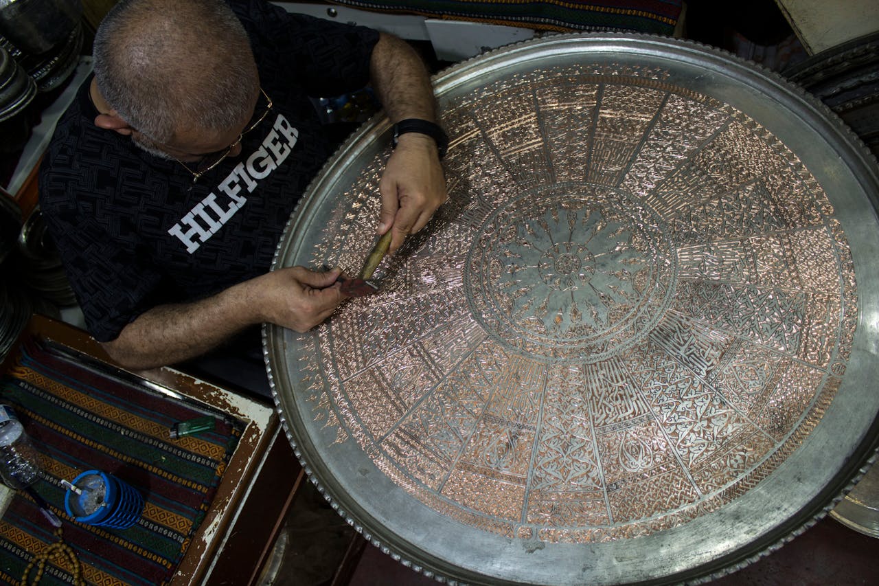 Skilled craftsman engraving intricate design on a large copper tray in Gaziantep, Türkiye