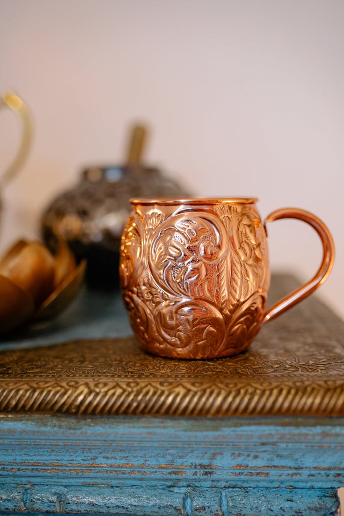 menu-17 Close-up of an intricately designed copper mug on a vintage table setting.